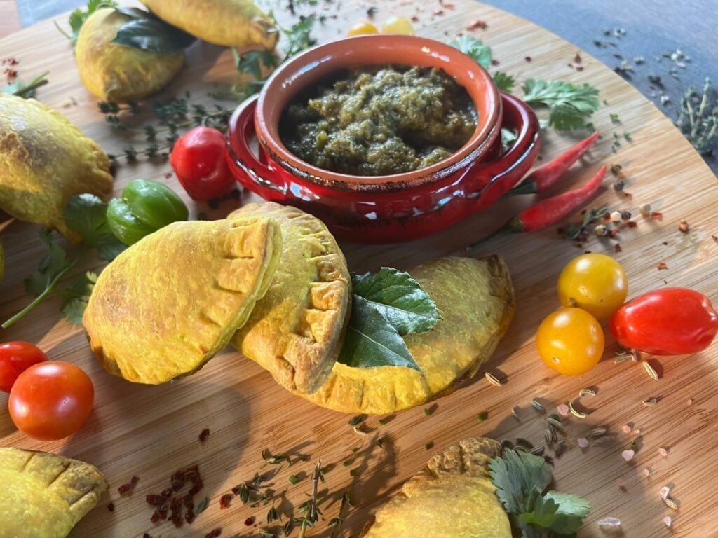 Caribbean patties served with green sauce, peppers, and herbs